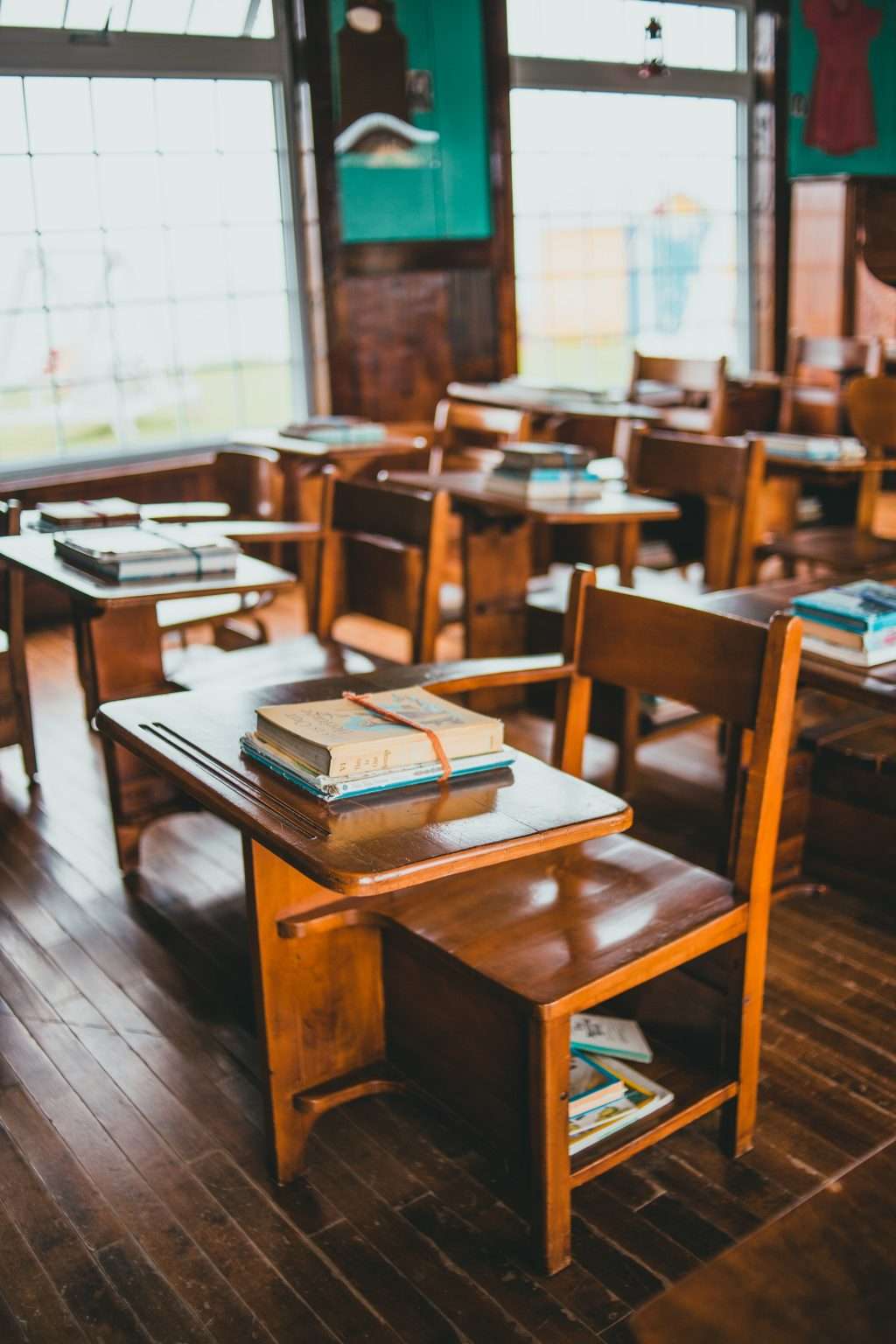 image from https://gulfbusiness.com/education-2-0-classrooms-need-a-voice-lift-to-adapt-to-the-new-normal/ this image includes a classroom. Empty and just with books on a desk